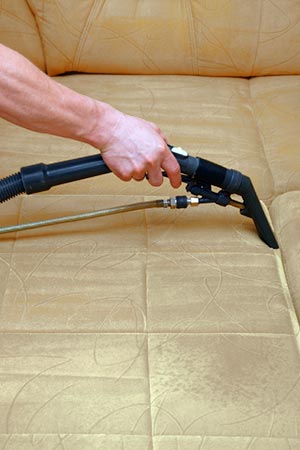 A handheld vaccuum is being used on a couch as part of fire cleanup services, done by The Whole Show Restorations.